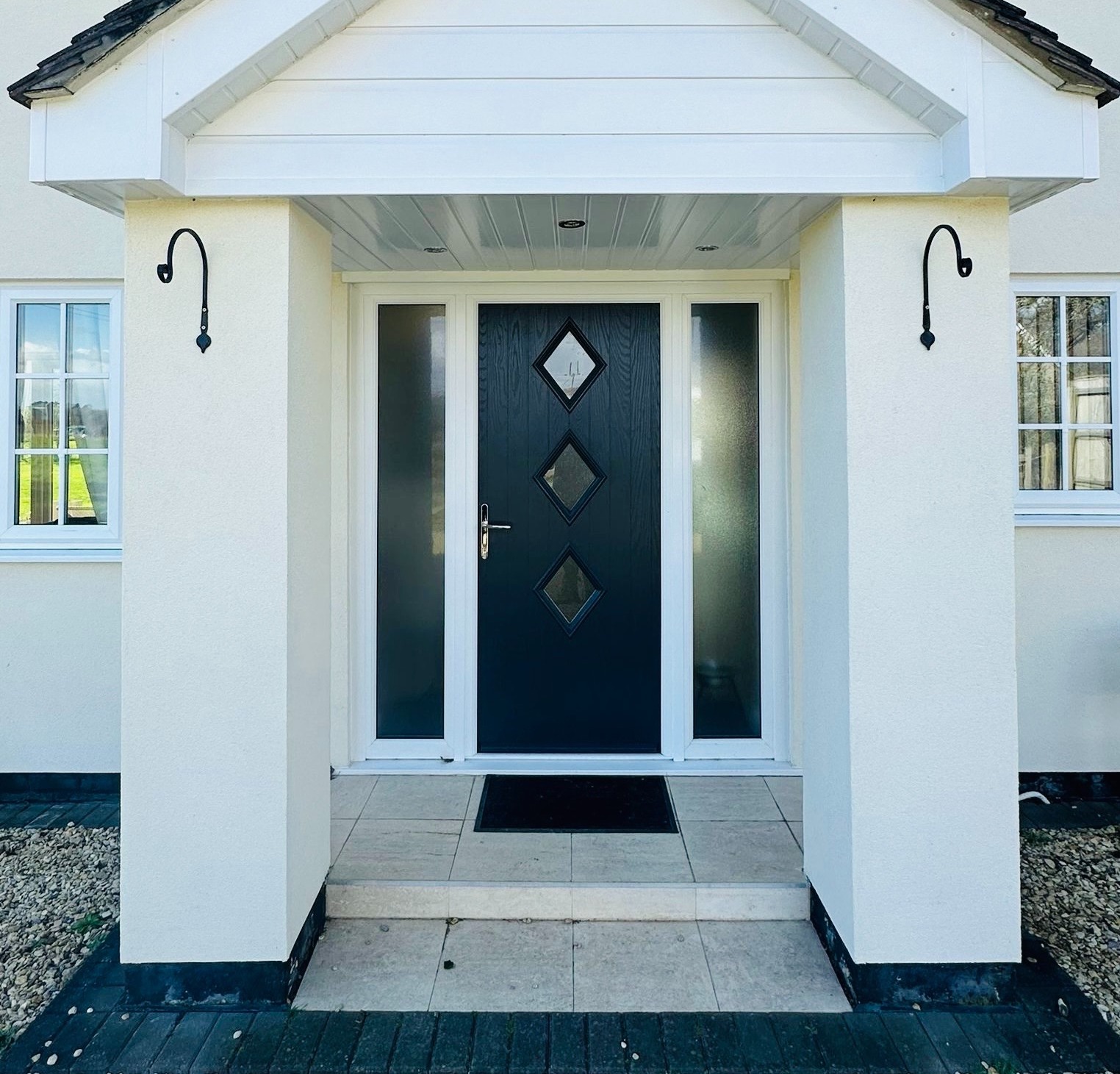 The front of a house in Dorset, with a white roofed porch and a black composite front door with two side panels. The facade looks modern and stylish.