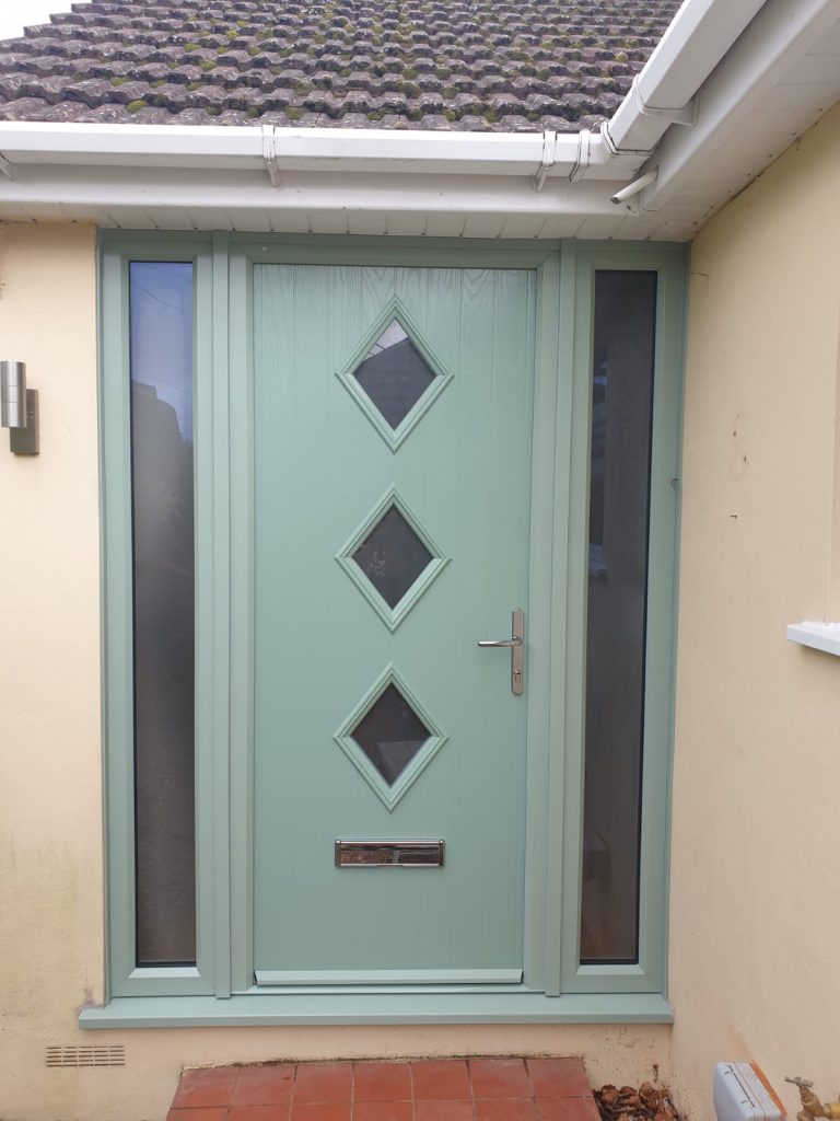 Front of a house with a sage green composite door, containing 3 triangular glass panels. The door gives the house a unique yet traditional look.